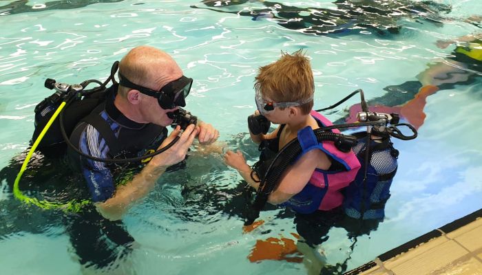 Een mannelijke instructeur geeft uitleg aan een jongen met betrekking tot persluchtduiken